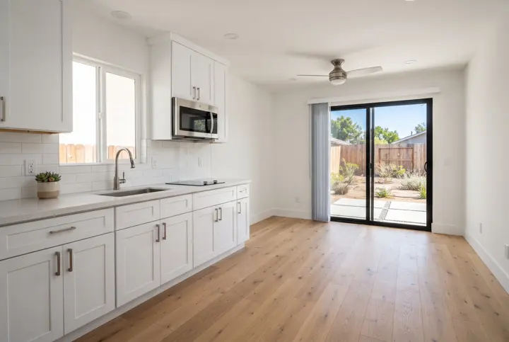 The interior of a compact ADU with a small modern kitchen along one wall with white shaker cabinets