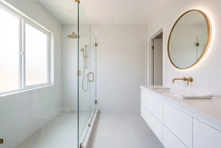 Bathroom with a white floating vanity, backlit round mirror and a walk-in glass shower