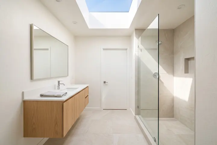Bathroom with a skylight, light oak floating vanity and a tiled walk-in shower