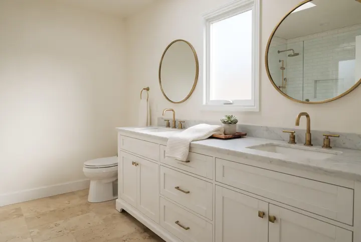 A primary bathroom with a long double-sink vanity in white cabinetry topped with a honed white marble countertop