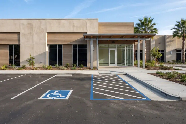 A van-accessible parking stall with a wide blue-striped hatched access aisle beside it and a smooth concrete curb ramp up to the sidewalk