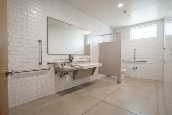 An accessible public restroom with a wall-mounted sink with clear knee space beneath