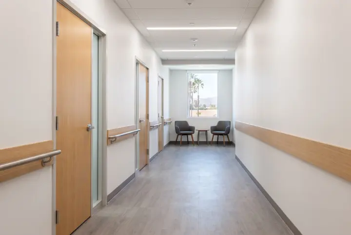 A medical suite corridor with light wood-tone doors with narrow glass sidelights