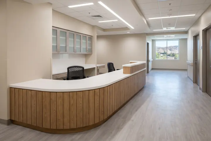 A nurse station with a long curved white solid-surface counter with a wood front panel