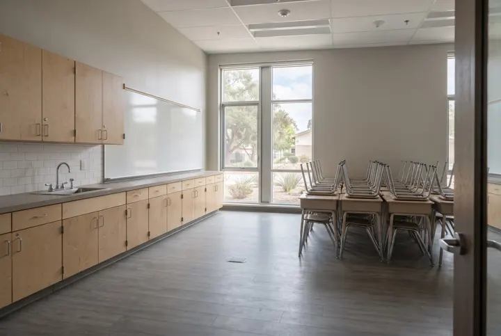 A renovated empty school classroom with new light wood casework cabinets and a sink counter along one wall