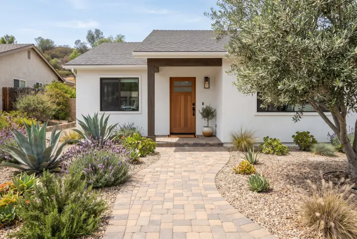 A curved paver walkway in warm tan and gray leading to a wood front door of a white stucco home