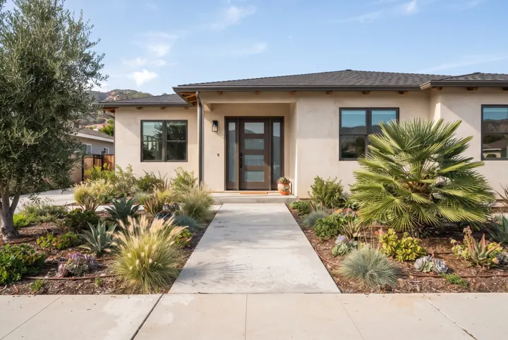 A straight light-gray concrete walkway with clean saw-cut joints leading to the front door of a modern stucco home