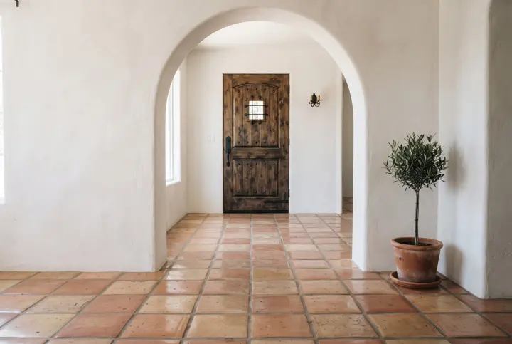 A Spanish-style home entry with warm terracotta Saltillo tile flooring, white plaster arched walls