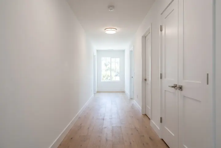 A long hallway with wide-plank natural oak flooring, white plaster walls