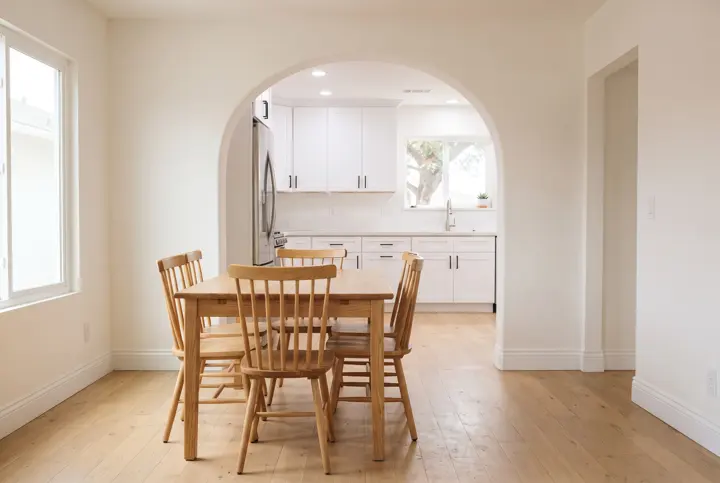 A smooth plaster arched doorway connecting a bright kitchen and a dining room