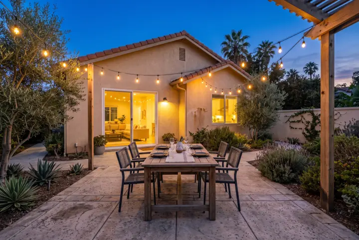 Backyard patio dining area with string lights at dusk in front of a stucco home