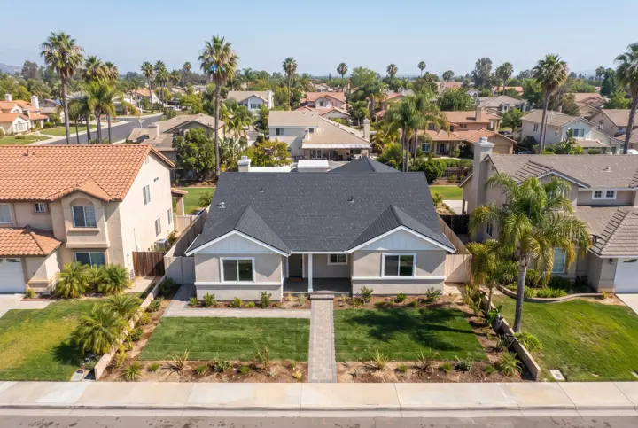 An aerial view from above of a Southern California suburban neighborhood with one home in the center having a brand-new clean roof in dark gray