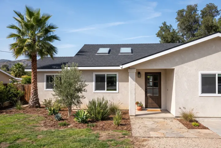 A stucco home with a new dark asphalt shingle roof and exactly two clean flat skylights with neat flashing set into the roof slope