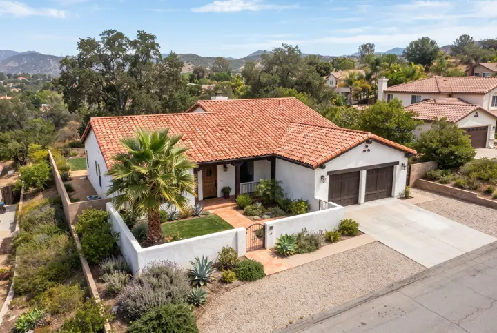 An aerial view from above and slightly to the side of a Spanish-style white stucco home with a new terracotta S-tile roof in warm orange tones with neat ridge caps
