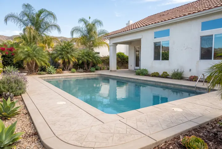 A stamped concrete pool deck in a light sand color with a stone-tile texture pattern and a smooth trowel-finish border