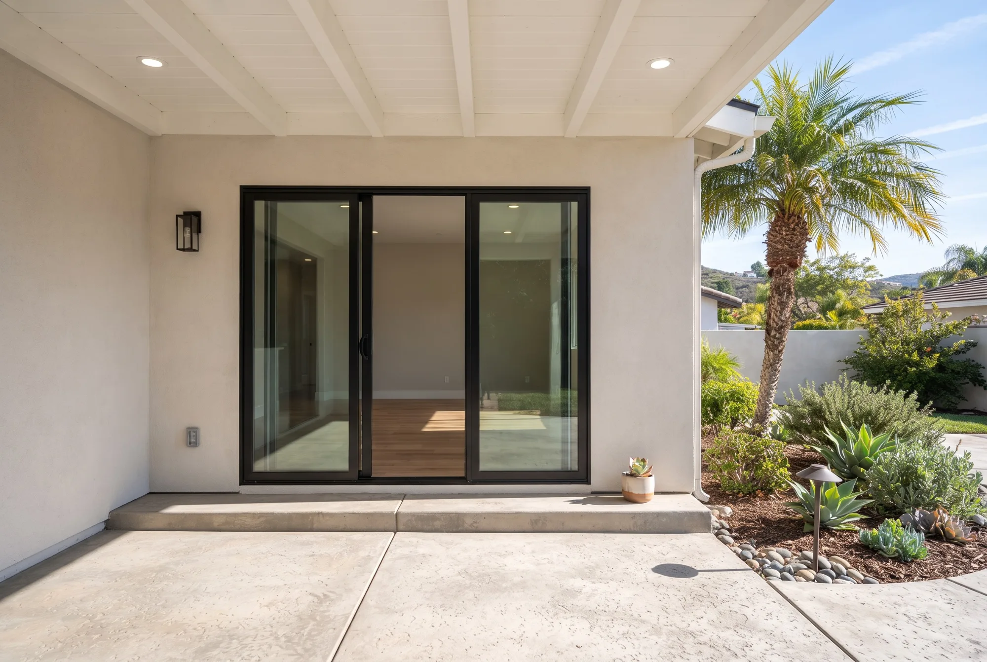 A stucco home with a black-framed sliding glass door opening to a concrete patio