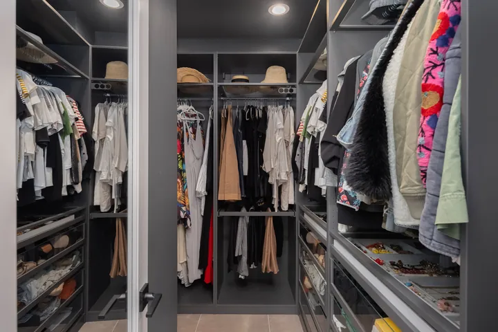 Walk-in primary closet with dark built-in shelving, hanging rails and drawers, interior design in Santa Clarita, CA, photo 17
